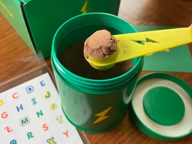 Scoop of Hiya Kids Daily Greens + Superfoods being mixed into oat milk – daily greens supplement for children