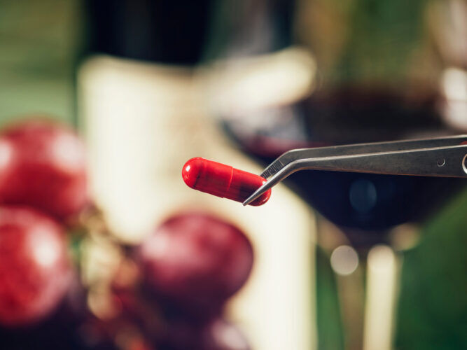 resveratrol supplement held by tweezers next to a glass of wine and fruit
