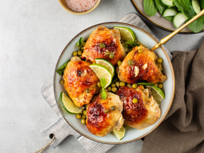 cooked chicken thighs on a plate with capers and limes