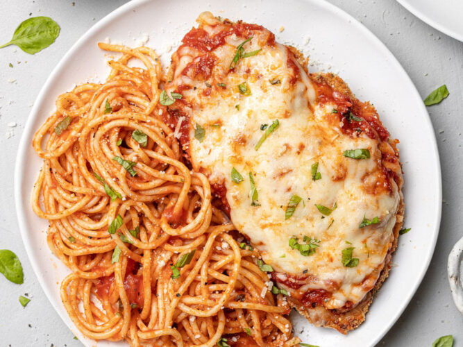 plate of chicken parmesan next to spaghetti with sauce