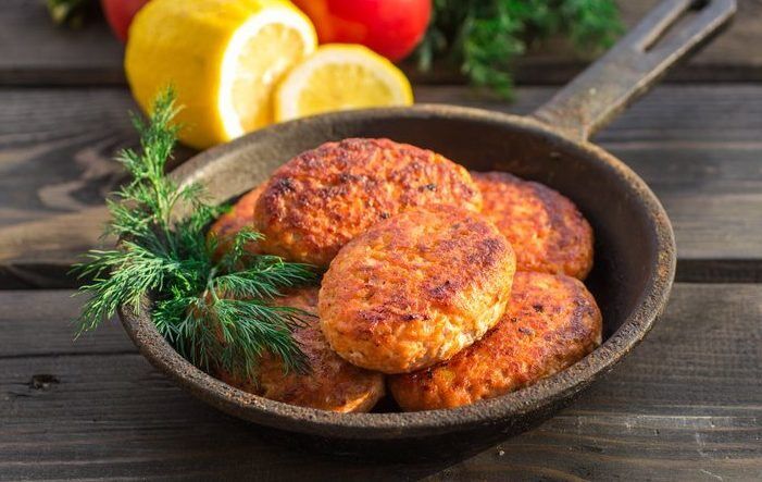 salmon fishcakes in a cast iron skillet, tomatoes and lemon