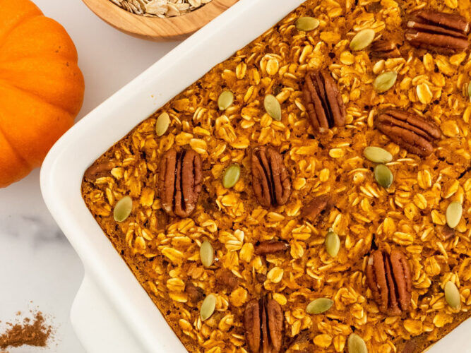 pumpkin pie baked oatmeal with seeds and nuts on top in a casserole dish