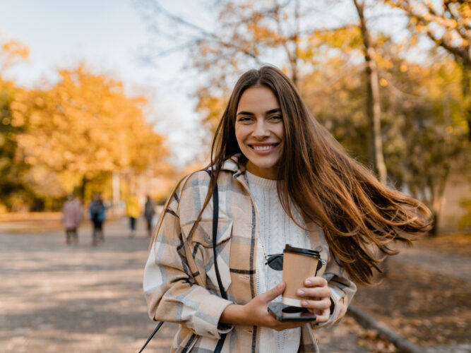 woman with healthy hair outside during the fall holding a coffee to go