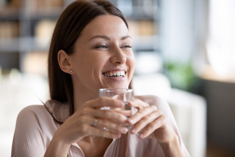 Smiling beautiful woman holding glass of pure mineral water close up; hydration helps lower blood sugar