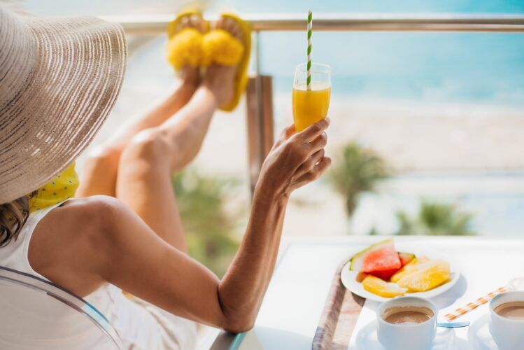 detail of a middle-aged woman with straw hat having breakfast on the terrace of a hotel and contemplating the sea. concept of relaxation and summer vacations in the mediterranean.