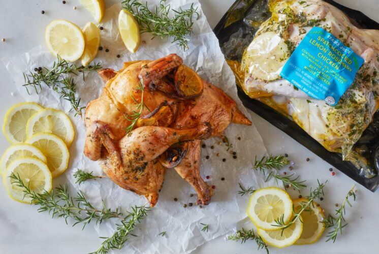 Trader Joe's Spatchcocked Lemon Rosemary Chicken, cooked and on parchment with lemon slices & wedges, fresh rosemary and peppercorns