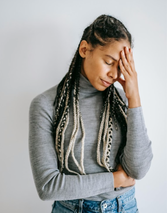 Woman with hand on forehead, eyes closed.